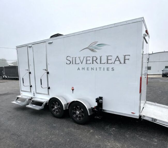 Rear side view of 17-foot ADA 3-station luxury restroom trailer with dual entry doors, metal steps, wheelchair access ramp, and dual axle wheels.