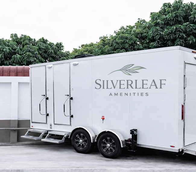 Luxury restroom trailer with dual doors, steps, and wheelchair ramp set up at a commercial property outdoor location.