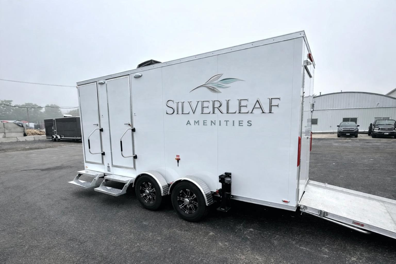 Rear side view of 17-foot ADA 3-station luxury restroom trailer with dual entry doors, metal steps, wheelchair access ramp, and dual axle wheels.
