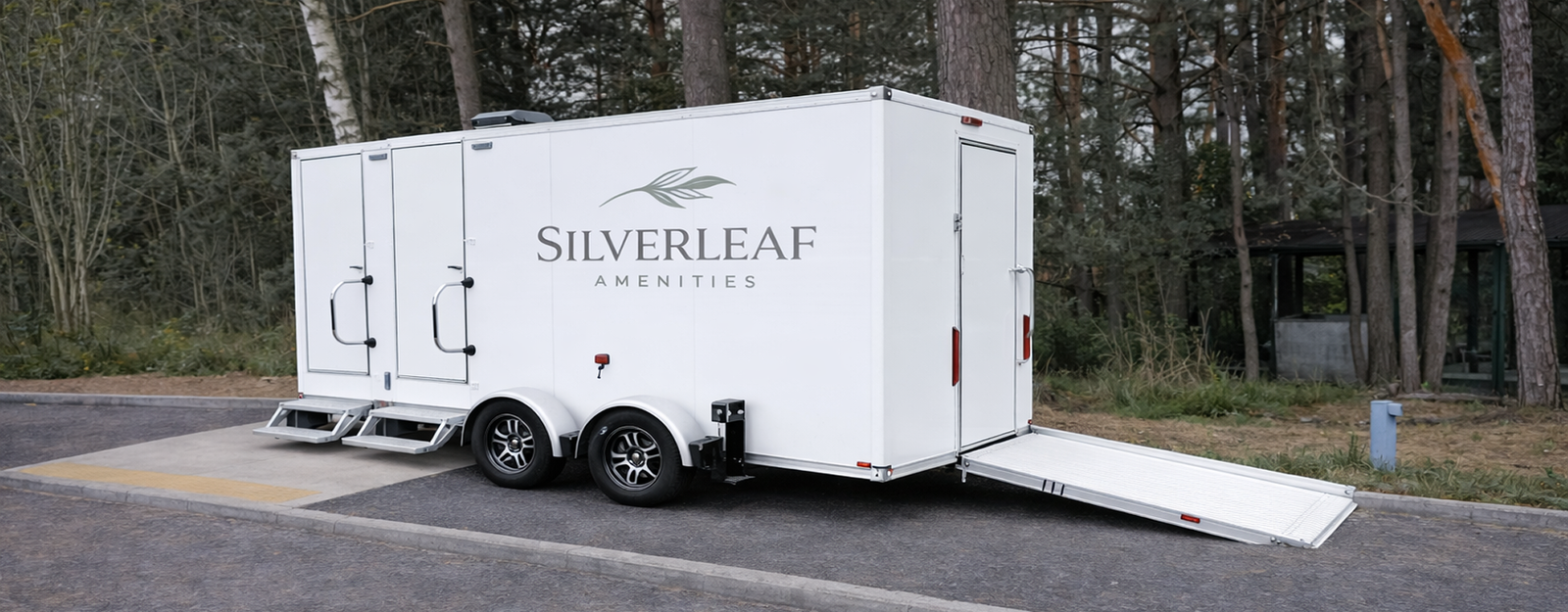 Rear side view of 17-foot ADA 3-station luxury restroom trailer with dual entry doors, metal steps, wheelchair access ramp, and dual axle wheels.